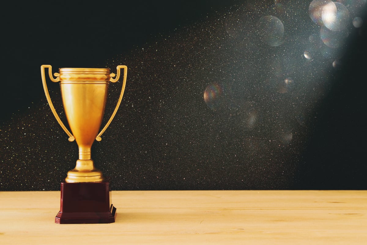 low key image of gold trophy over wooden table and dark background, with abstract glitter lights.